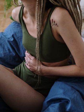 Woman sitting in bed holding her stomach, indicating pain or discomfort, possibly due to cramps.