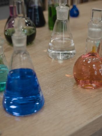 Colorful laboratory flasks with various liquids on a wooden desk for science experiments.